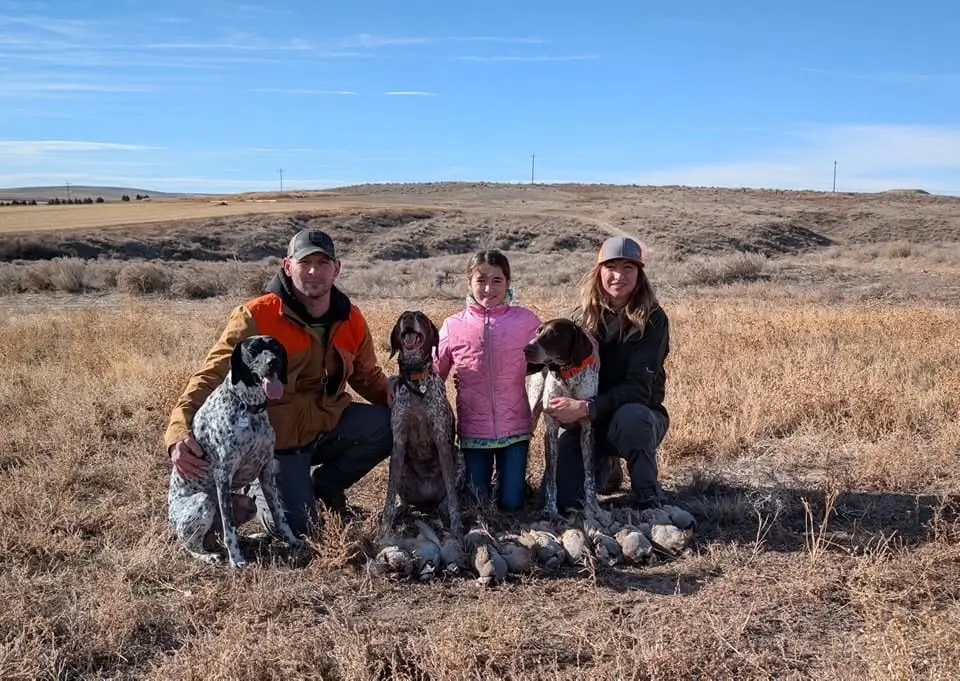 A family poses with their hunting dogs and harvested chukar in a field.