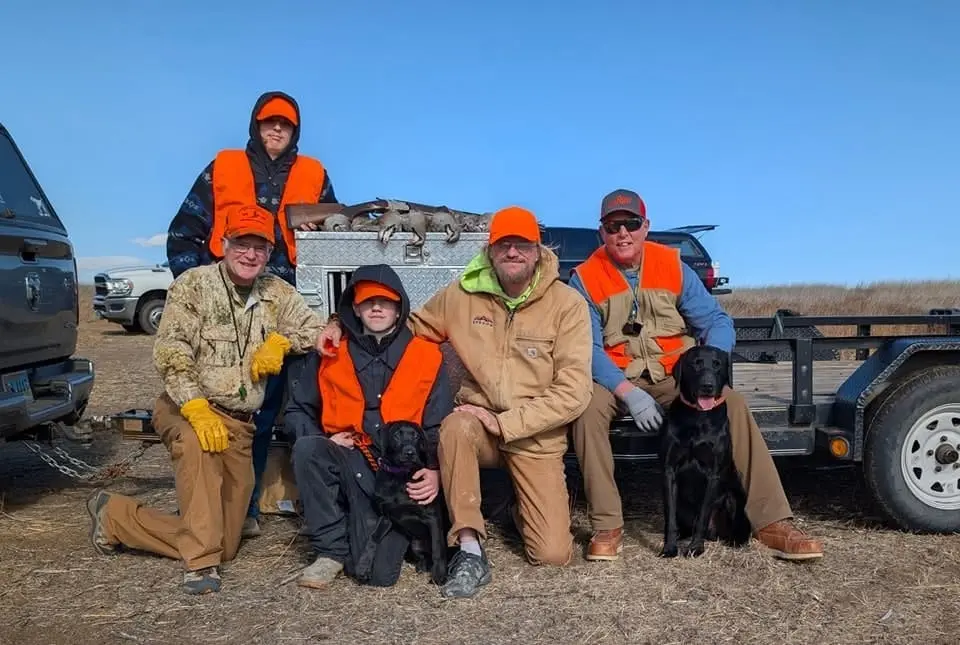 A group of hunters and their dogs pose with harvested chukar on a trailer.