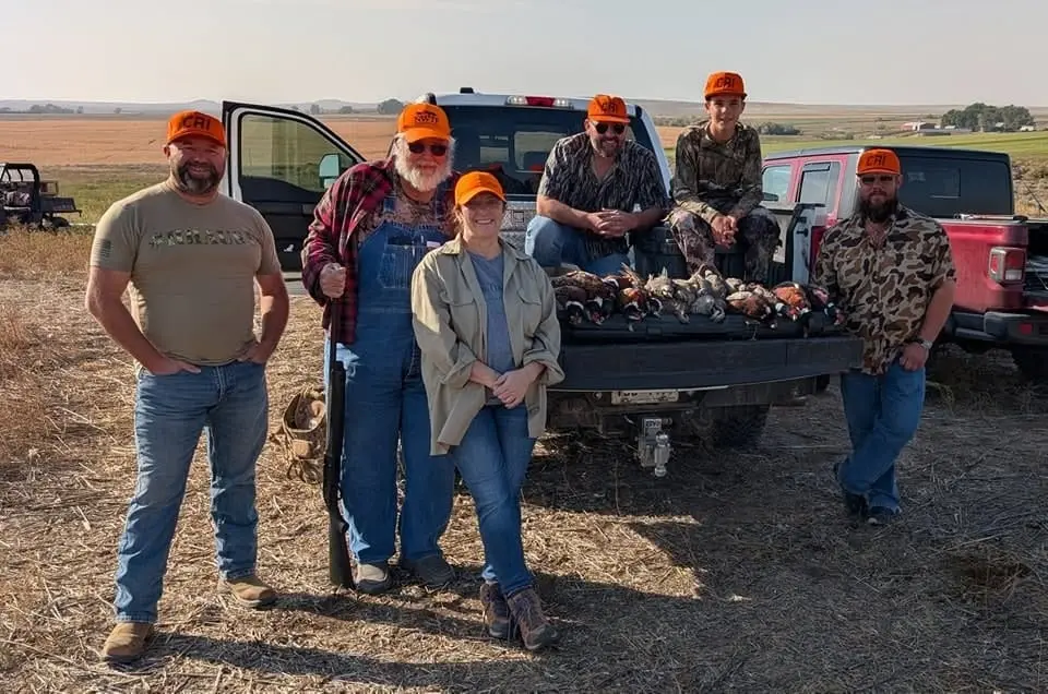 A group of hunters poses with their harvested birds in the back of a pickup truck.