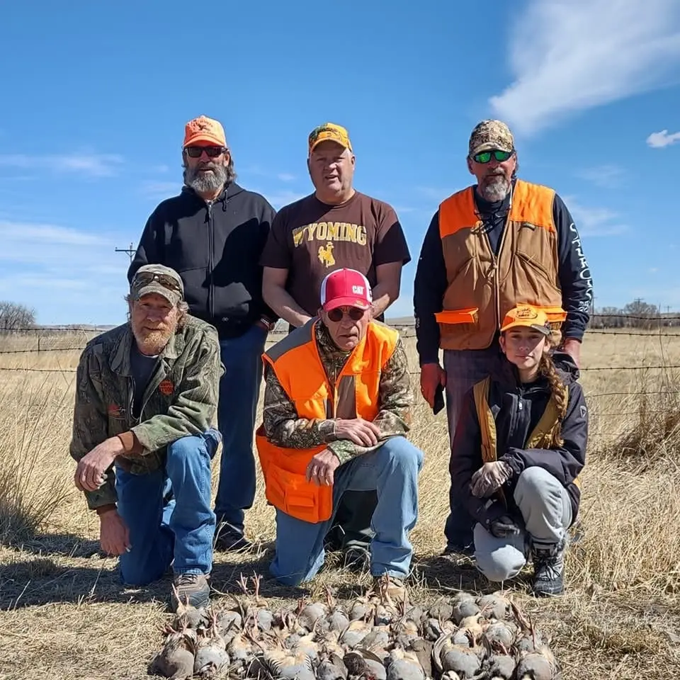 A group of hunters, including a child, pose with their harvested chukar partridges in a field.