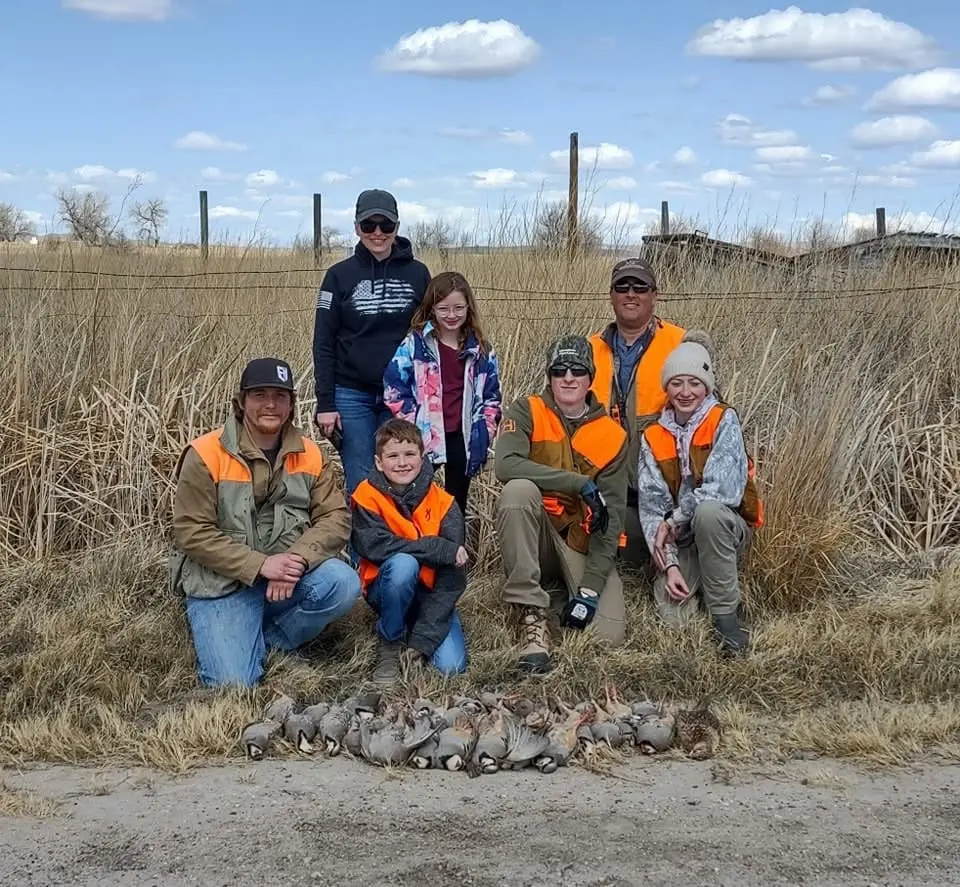 A group of hunters, including children, pose with their harvested chukar partridges in a field.