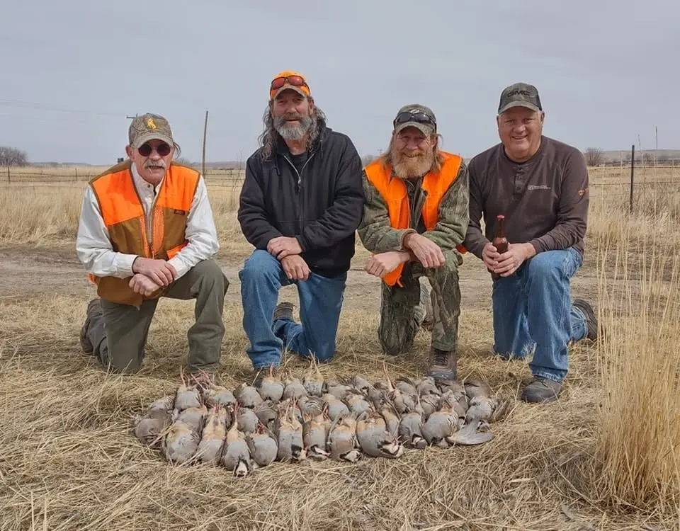 Four hunters kneel in a field with their harvest of birds.