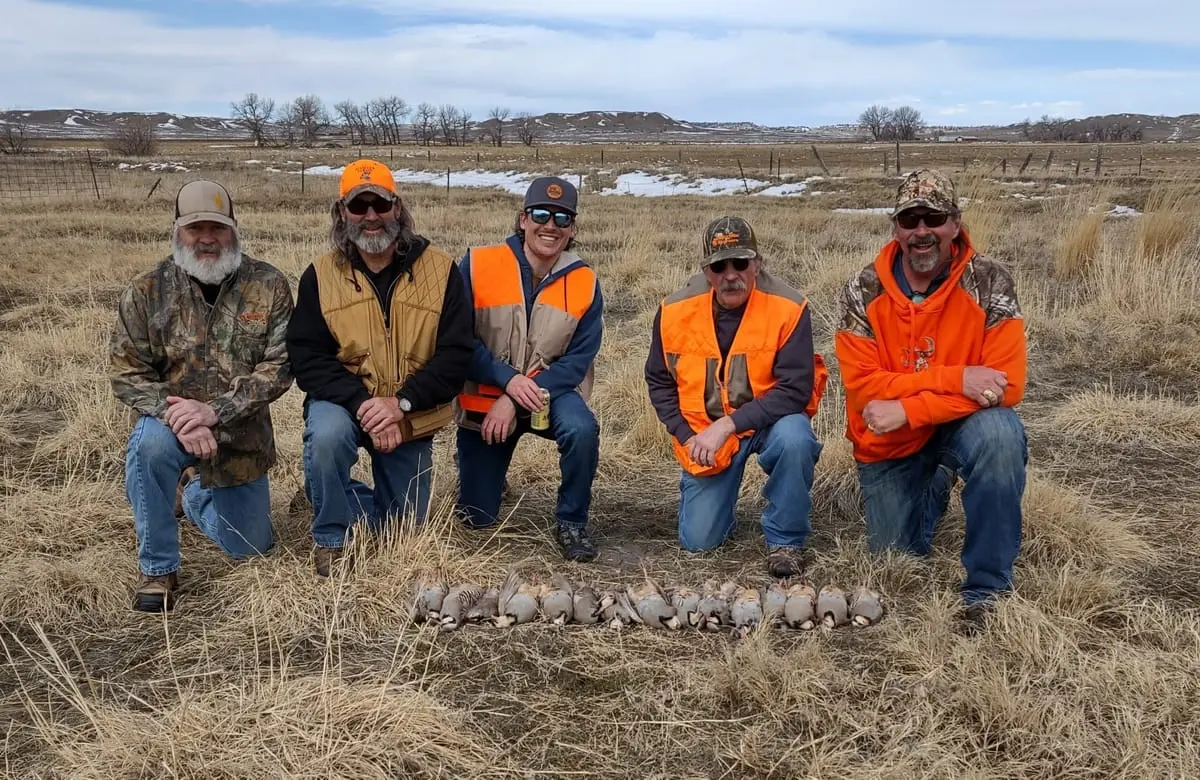 Five hunters kneel in a field with their harvested chukar partridges.