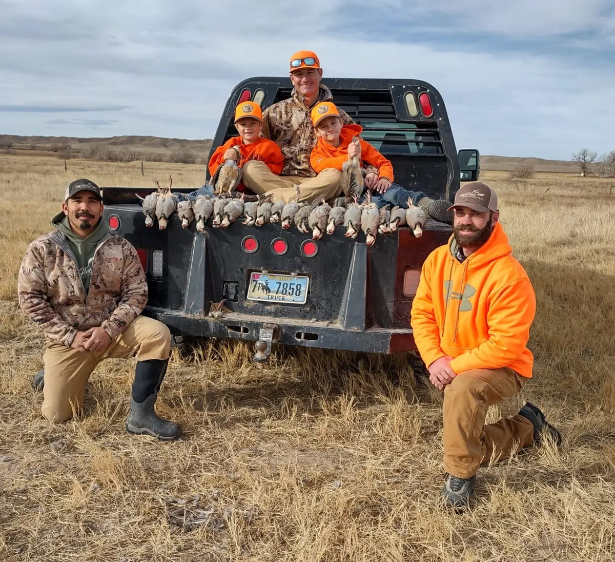 Hunters pose with harvested chukar partridges in the back of a pickup truck.