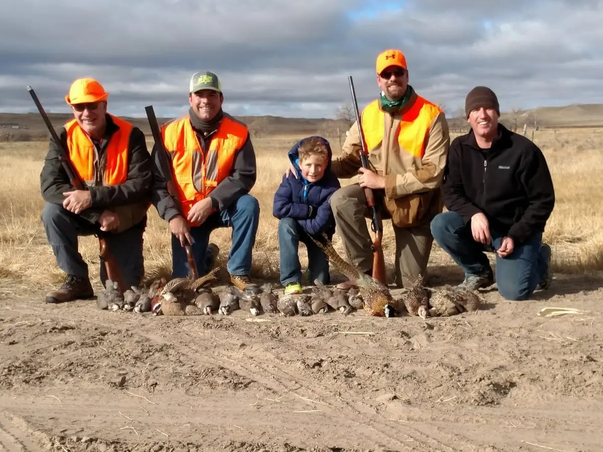 Four men and a child pose with harvested pheasants and chukar in a field.