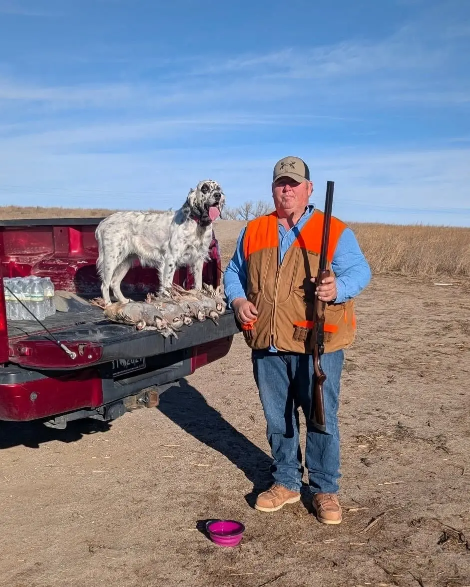 A hunter and a dog pose with harvested chukar in the back of a truck.
