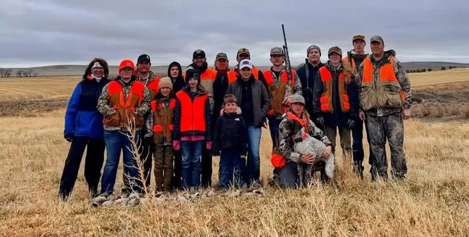 A group of hunters and children pose in a field with a hunting dog.