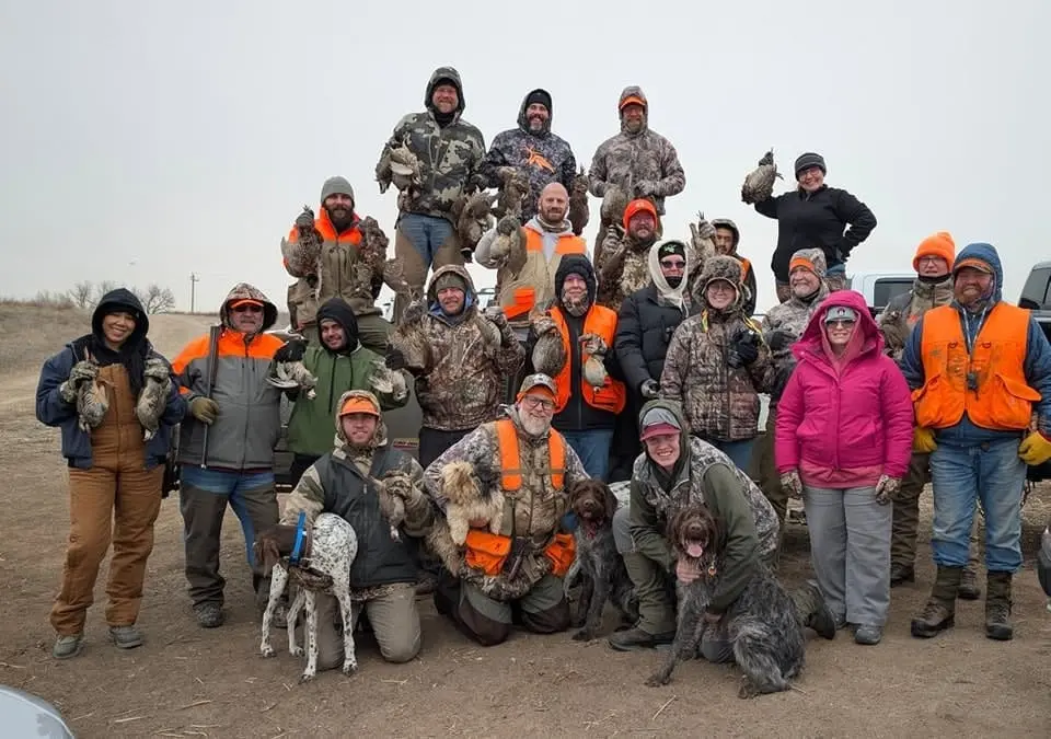 A large group of hunters and their hunting dogs pose with harvested pheasants and chukar.
